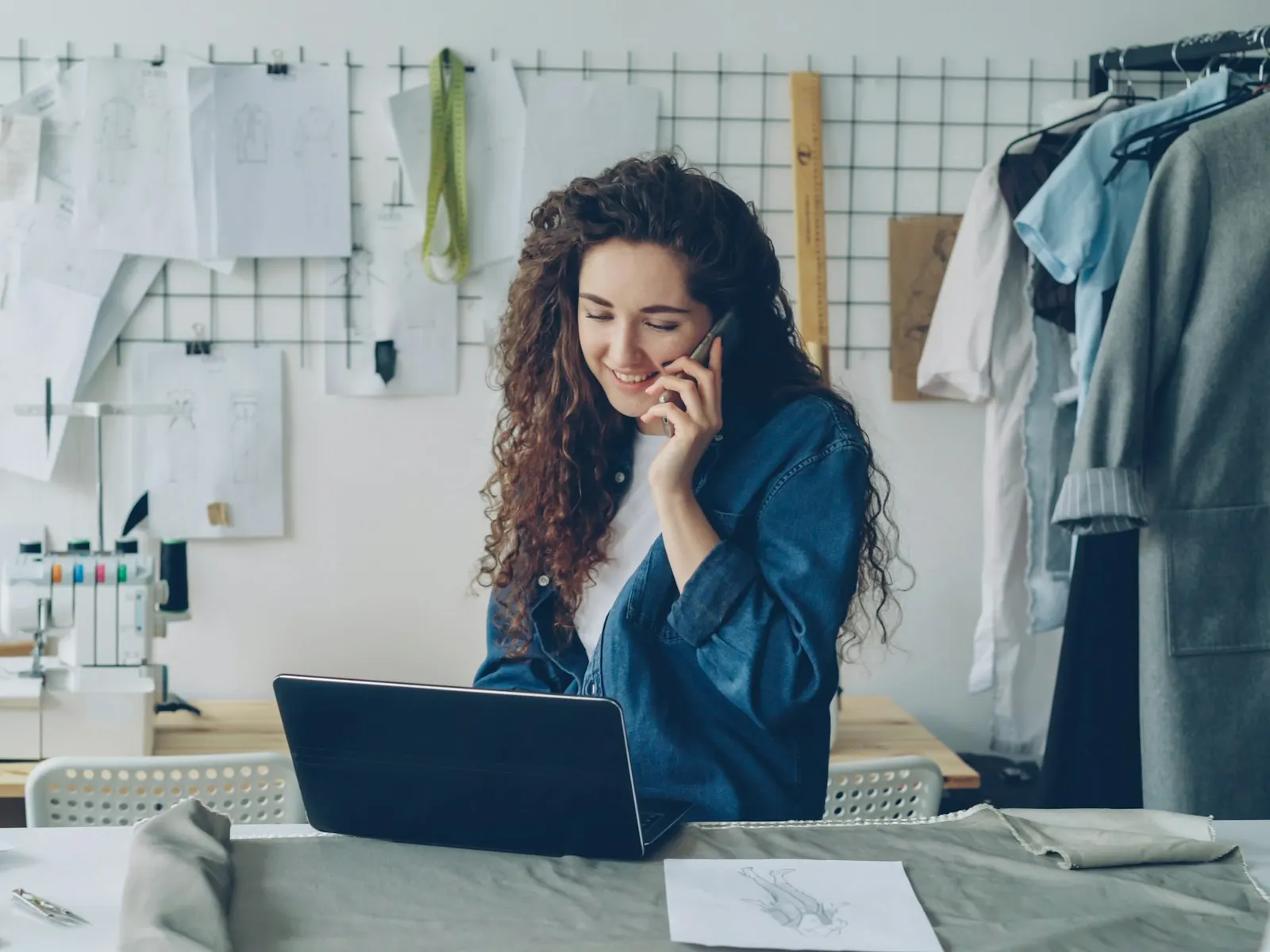Business owner in her studio on the phone with a customer while working on her laptop